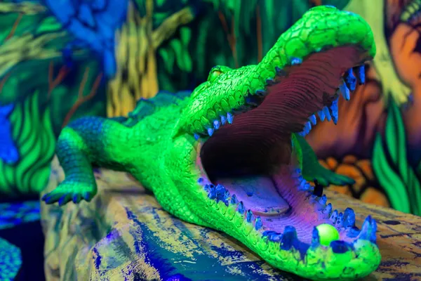 Großes leuchtendes Krokodil mit offenem Maul neben einer Minigolfbahn