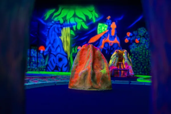 Minigolfbahn vor einer leuchtenden Felslandschaft mit Vulkan und Figuren