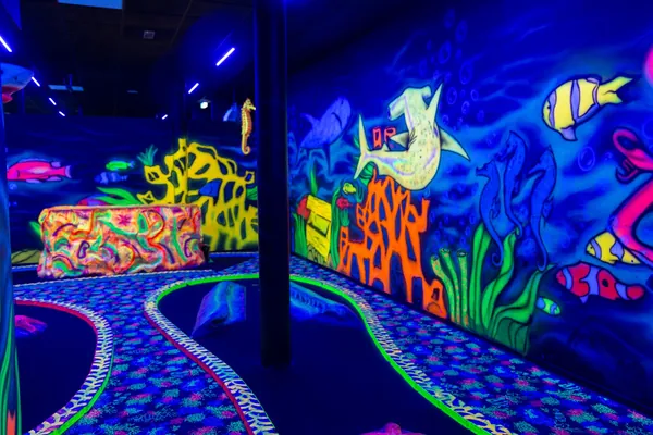 Schwarzlicht-Minigolfbahn in der Unterwasserwelt mit leuchtenden Korallen und Fischen
