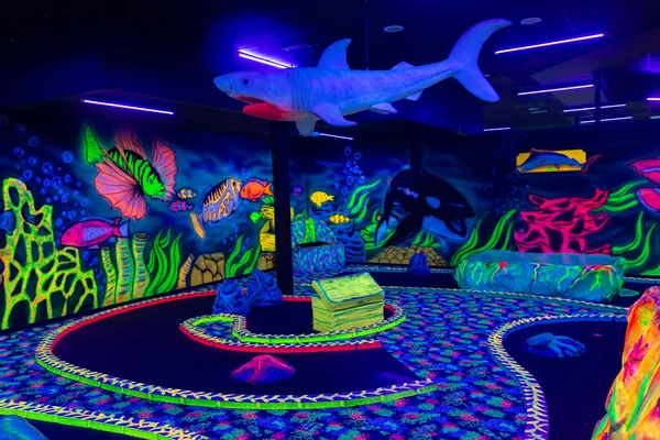 Ein großer Hai schwebt über der Minigolfbahn, ringsum leuchtende Korallen